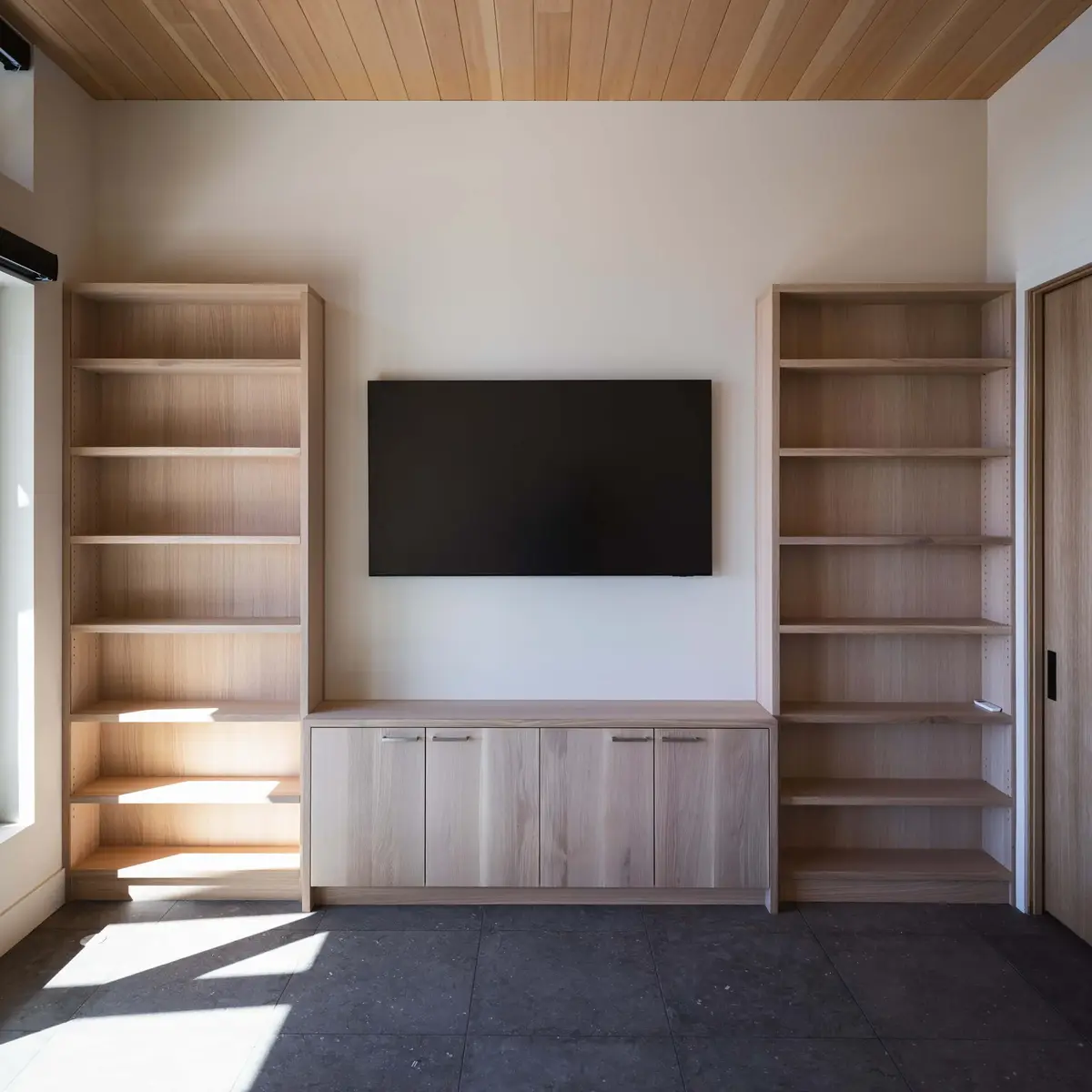 Built in shelving either side of a wall mounted screen above a low cabinet