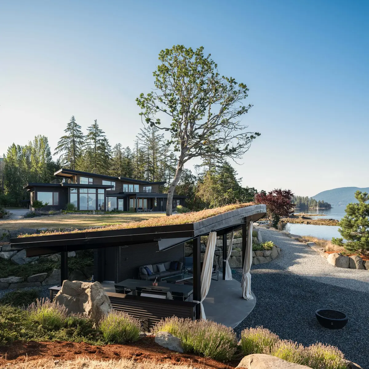 The house across a planted rock garden, shed roofs stepping down toward the water
