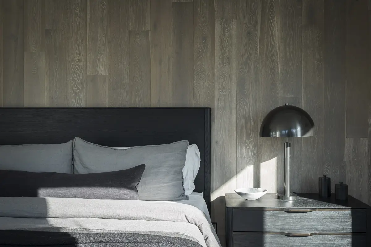 Bed against a wood panelled wall, a domed lamp on the nightstand in sun