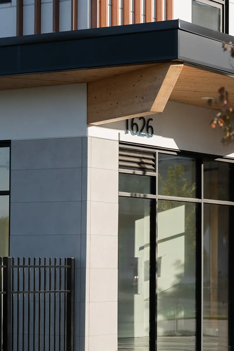Address numerals on a white panel wall below a wood soffit, glass entry doors alongside