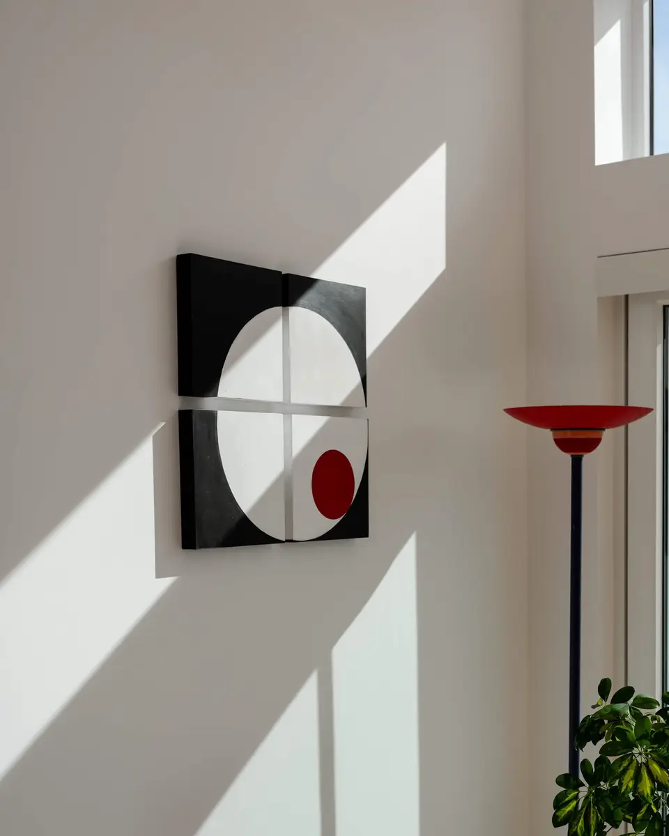 A sunbeam crossing the white wall past a black and red circle panel