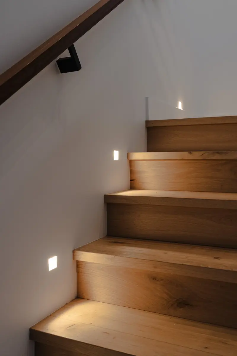 Recessed lights washing warm light across wood stair treads in a white stairwell