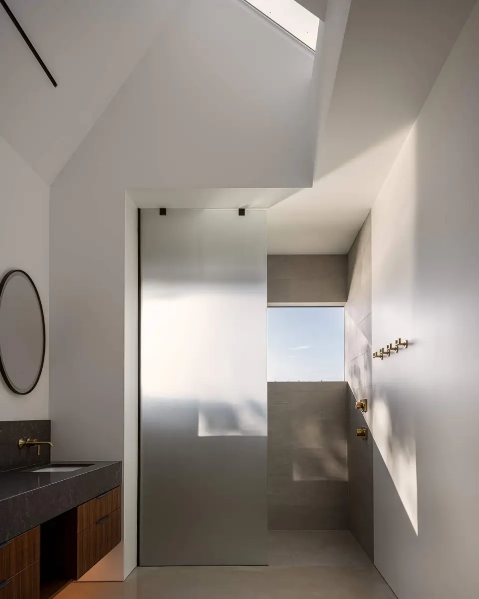 Ensuite under a skylit slope, a frosted glass screen beside a grey tiled shower