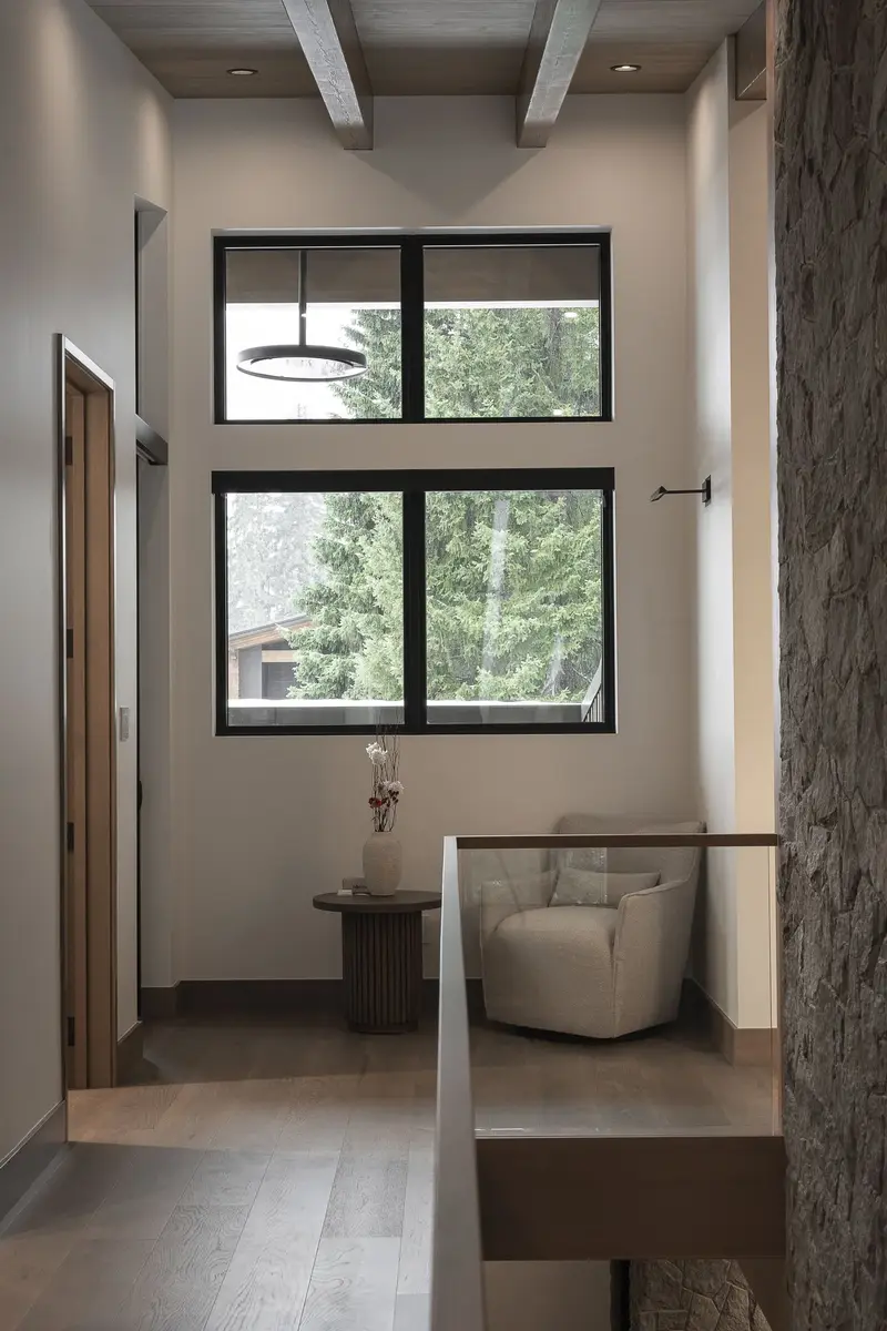 Hallway under dark ceiling beams to a window, a chair and round table at the end