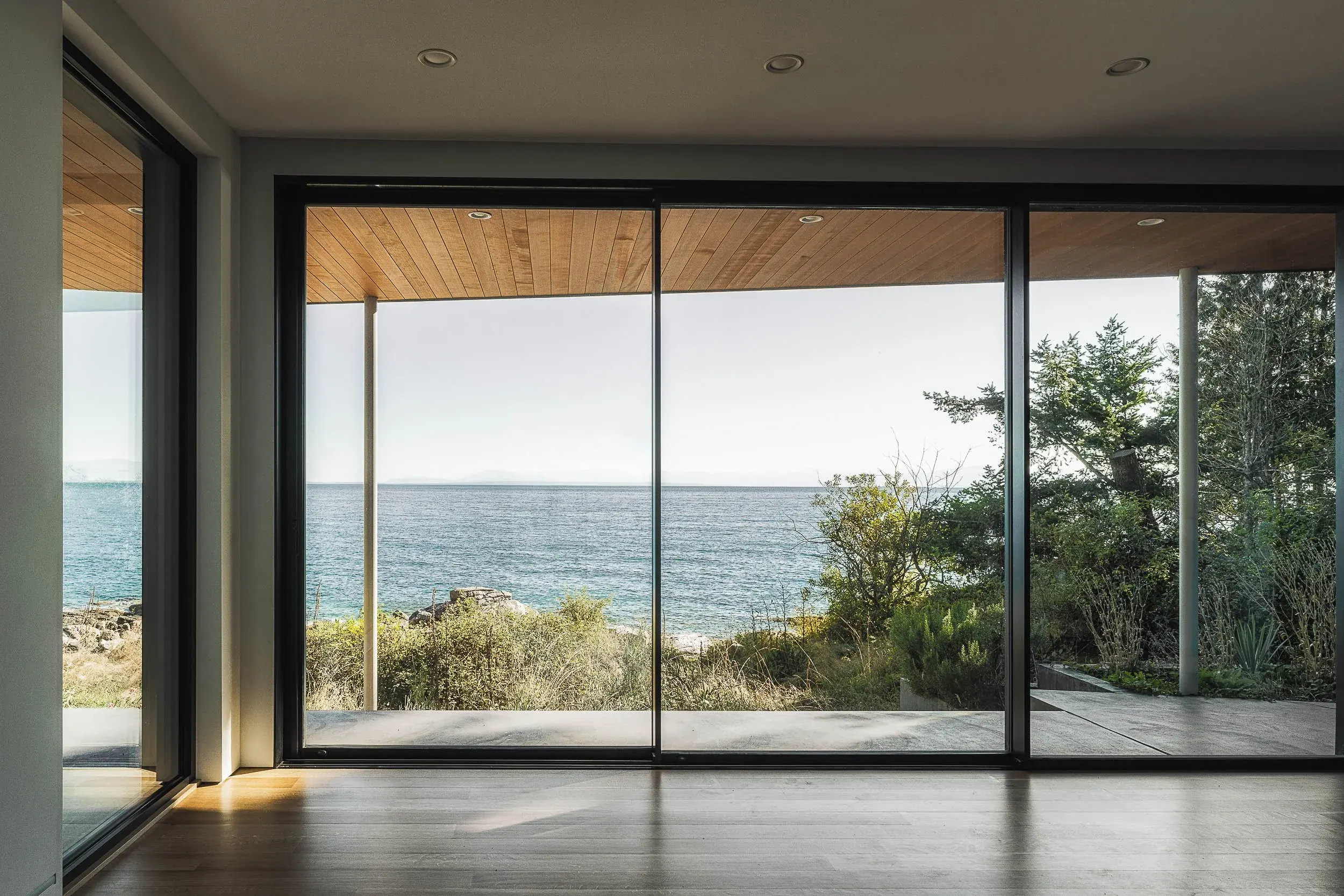 Living room with a full width slider open to the water, wood soffit beyond