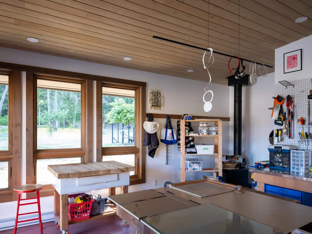 Workshop with hand tools on a pegboard, a wood stove and a bench under the windows