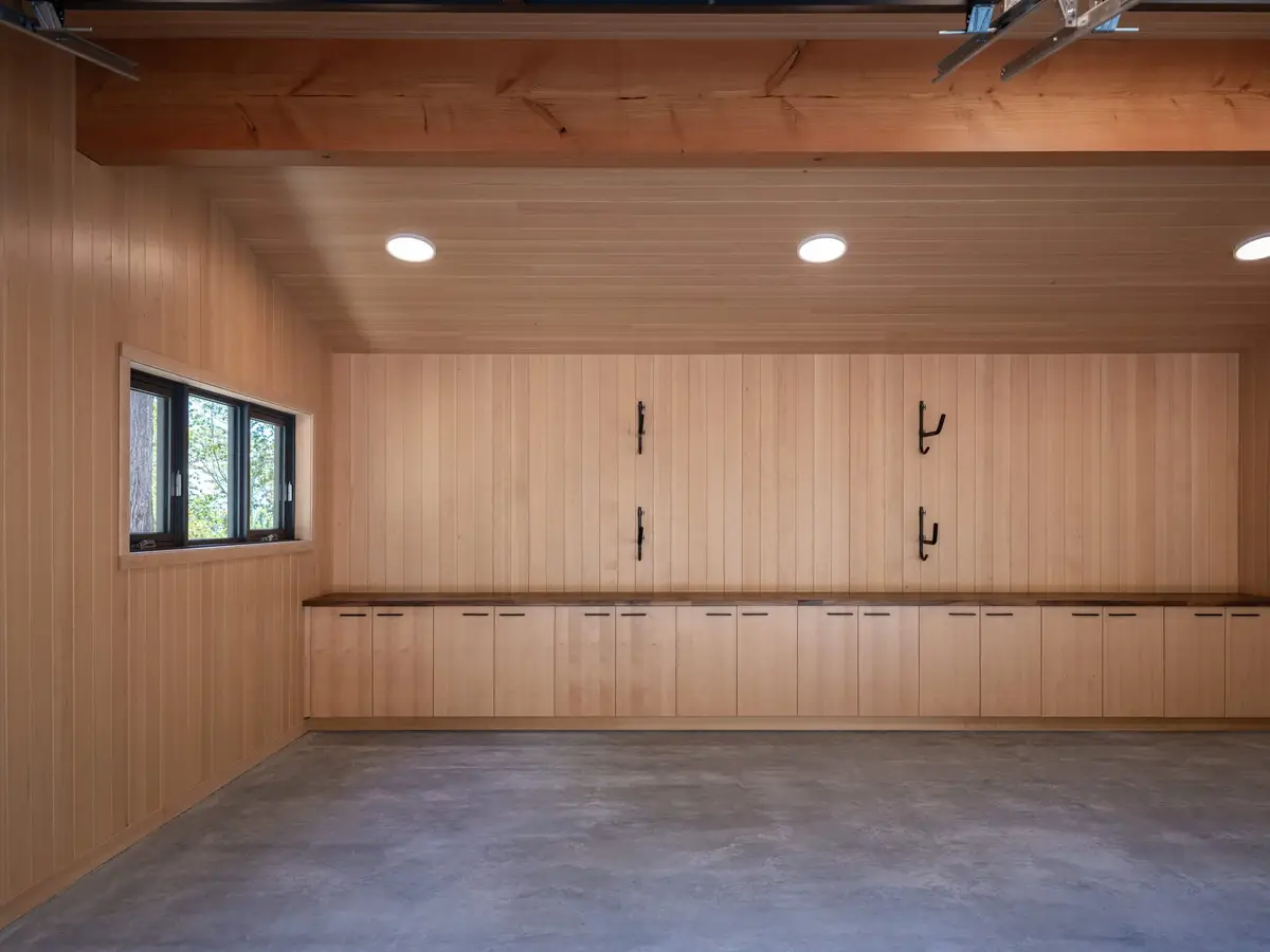 Long run of wood cabinets under a counter with wall hooks above, concrete floor