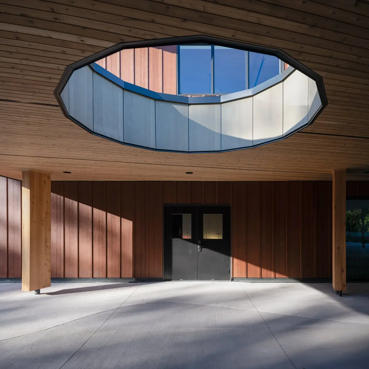 An oval opening cut through the wood soffit of the covered entry, clerestory glazing above