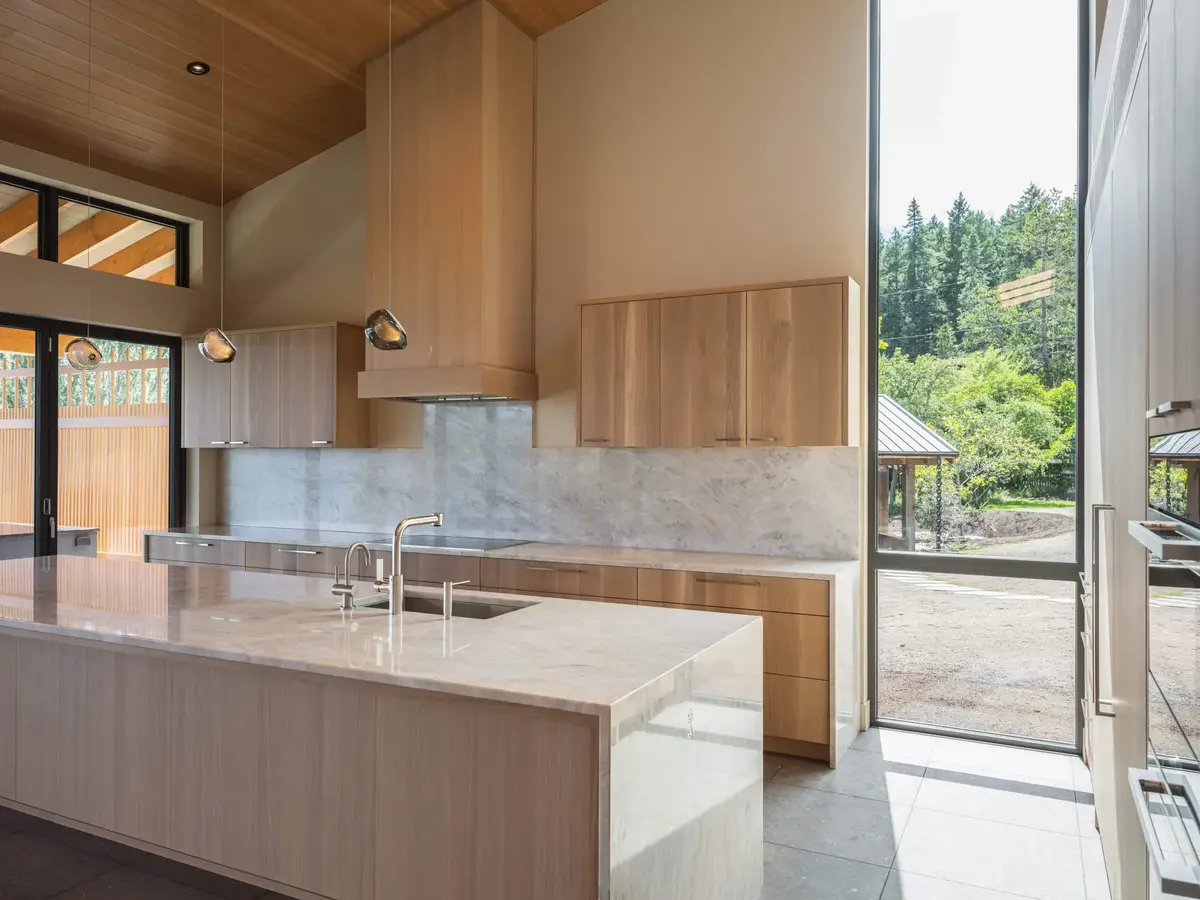 Stone island under two pendants, the kitchen opening to glazing and the trees beyond