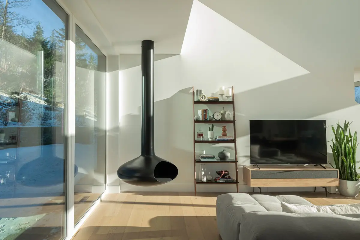 Living room corner with a suspended black fireplace, glazing onto a snowy forested slope