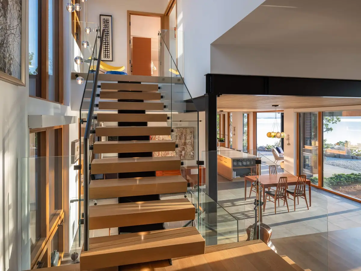 Looking up an open timber stair, the dining table and glazing beyond