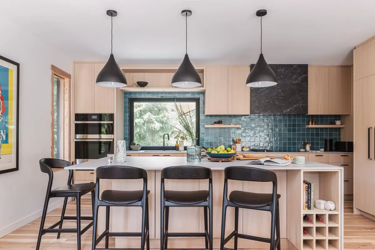Kitchen island with four black stools under three black pendants, blue green tile behind