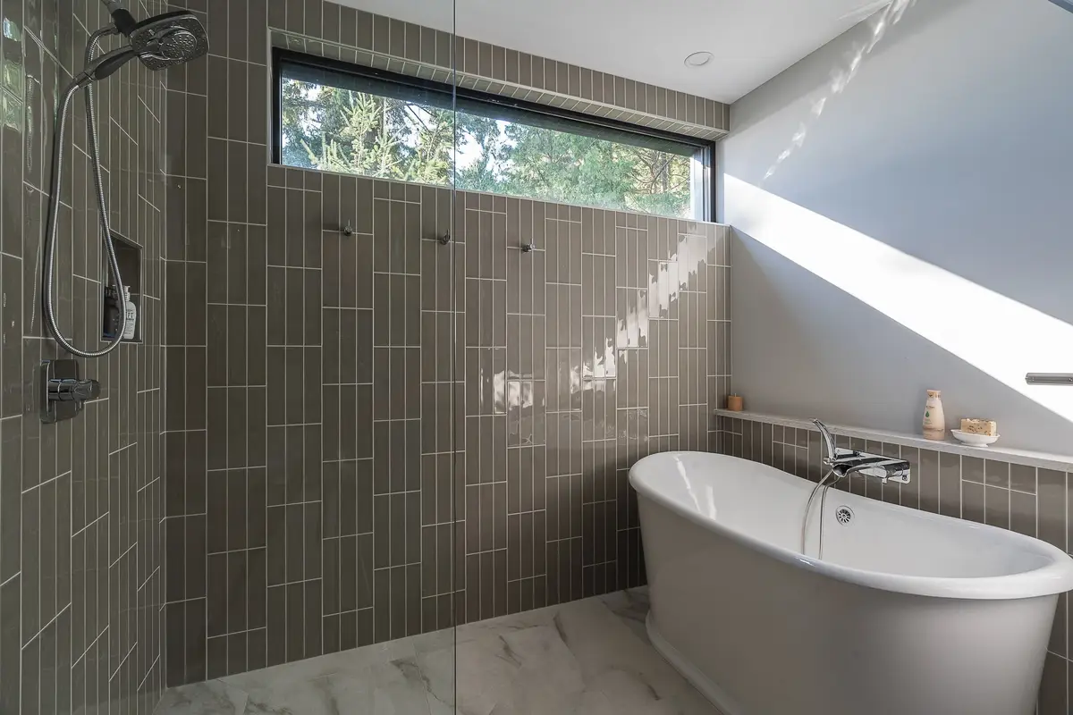 Freestanding tub under a long clerestory window, tiled walls and a pale veined floor