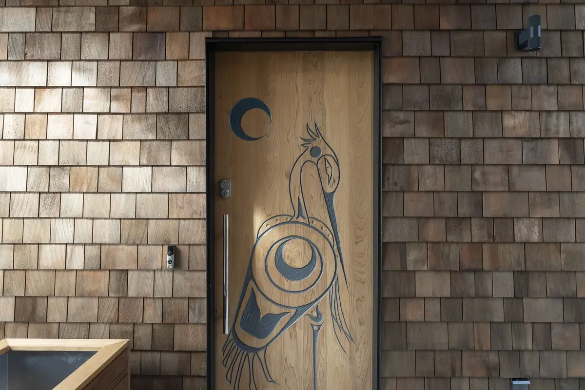 A wood entry door carved with a bird and moon motif in a shingled wall