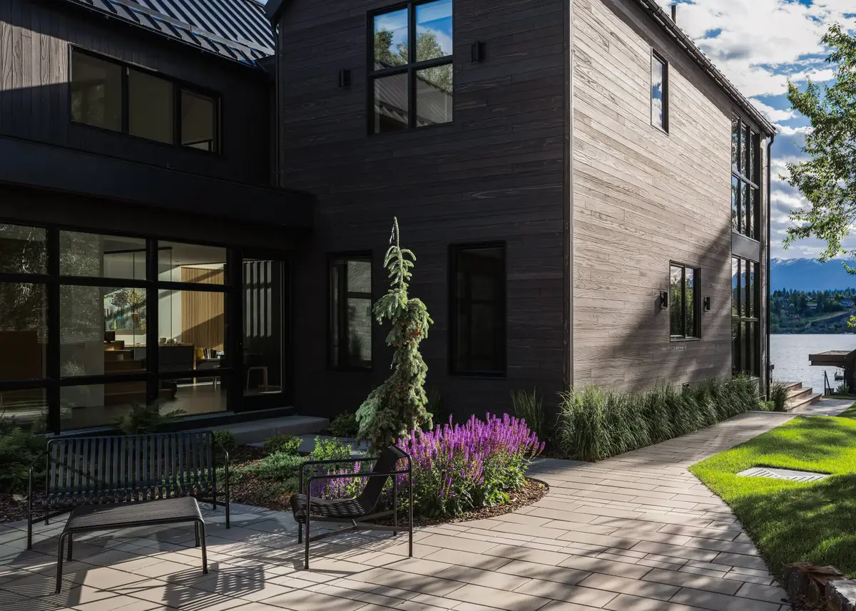 Courtyard corner where dark siding meets pale grey boards, the lake beyond the lawn