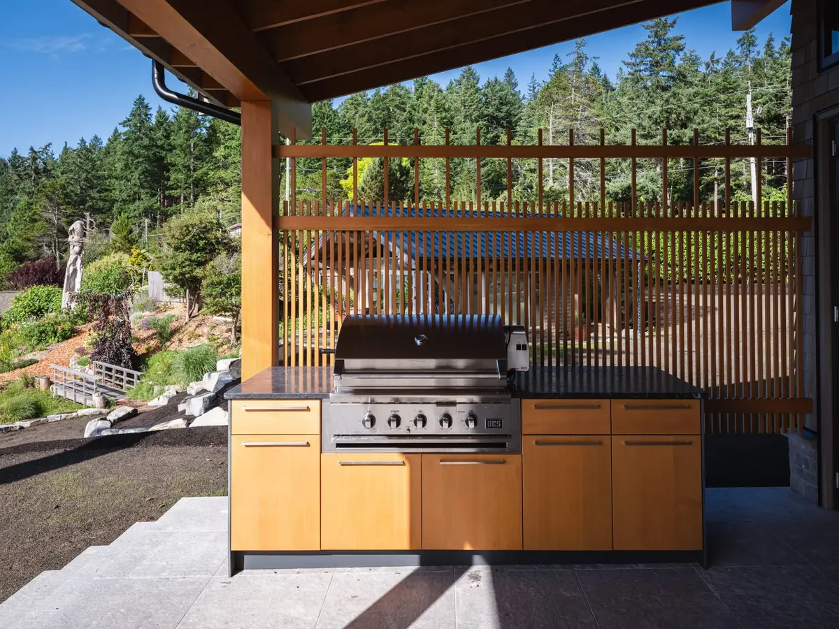Grill and wood cabinets on a covered terrace, a slatted screen open to the garden