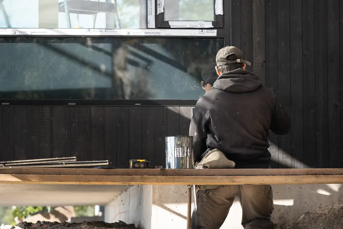 A tradesperson fitting dark vertical siding on a house under construction