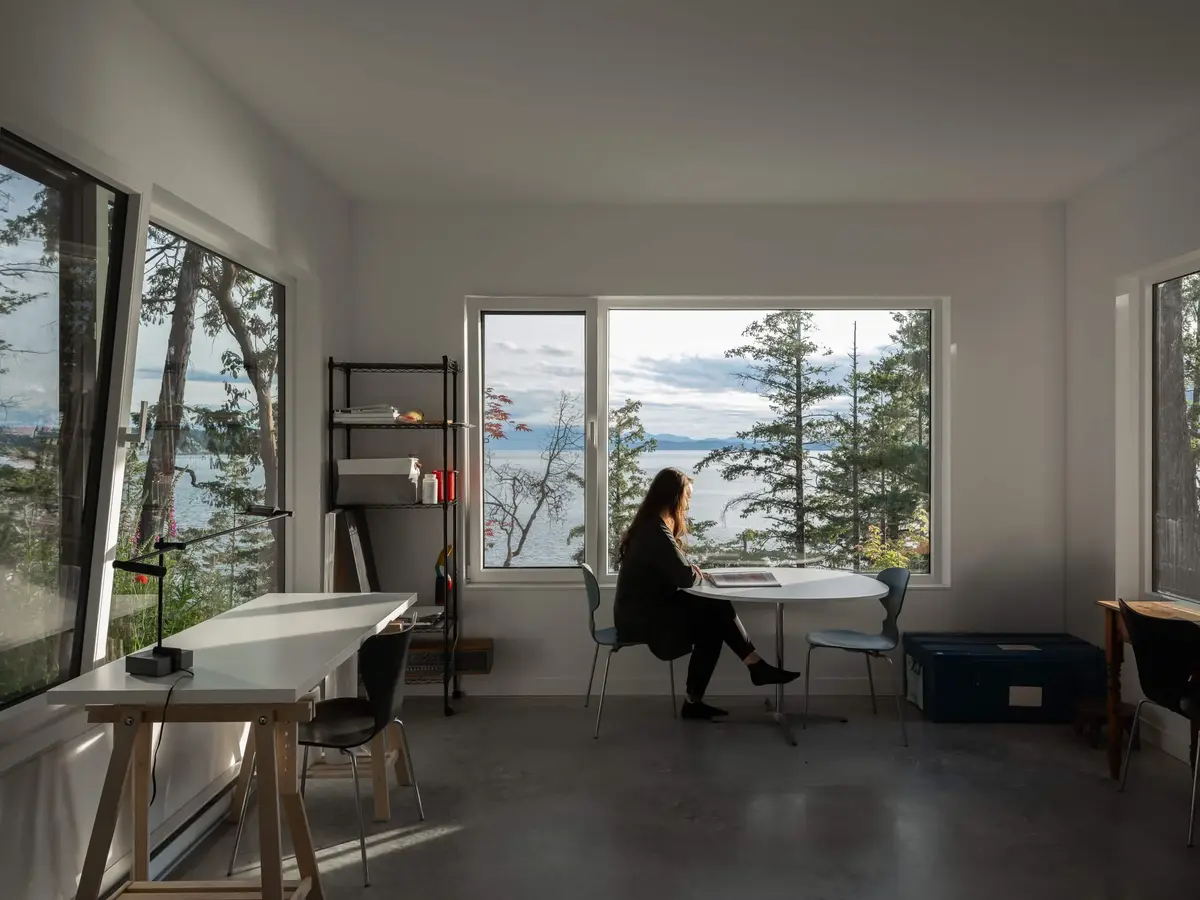 A studio with picture windows onto the water, someone working at the far table