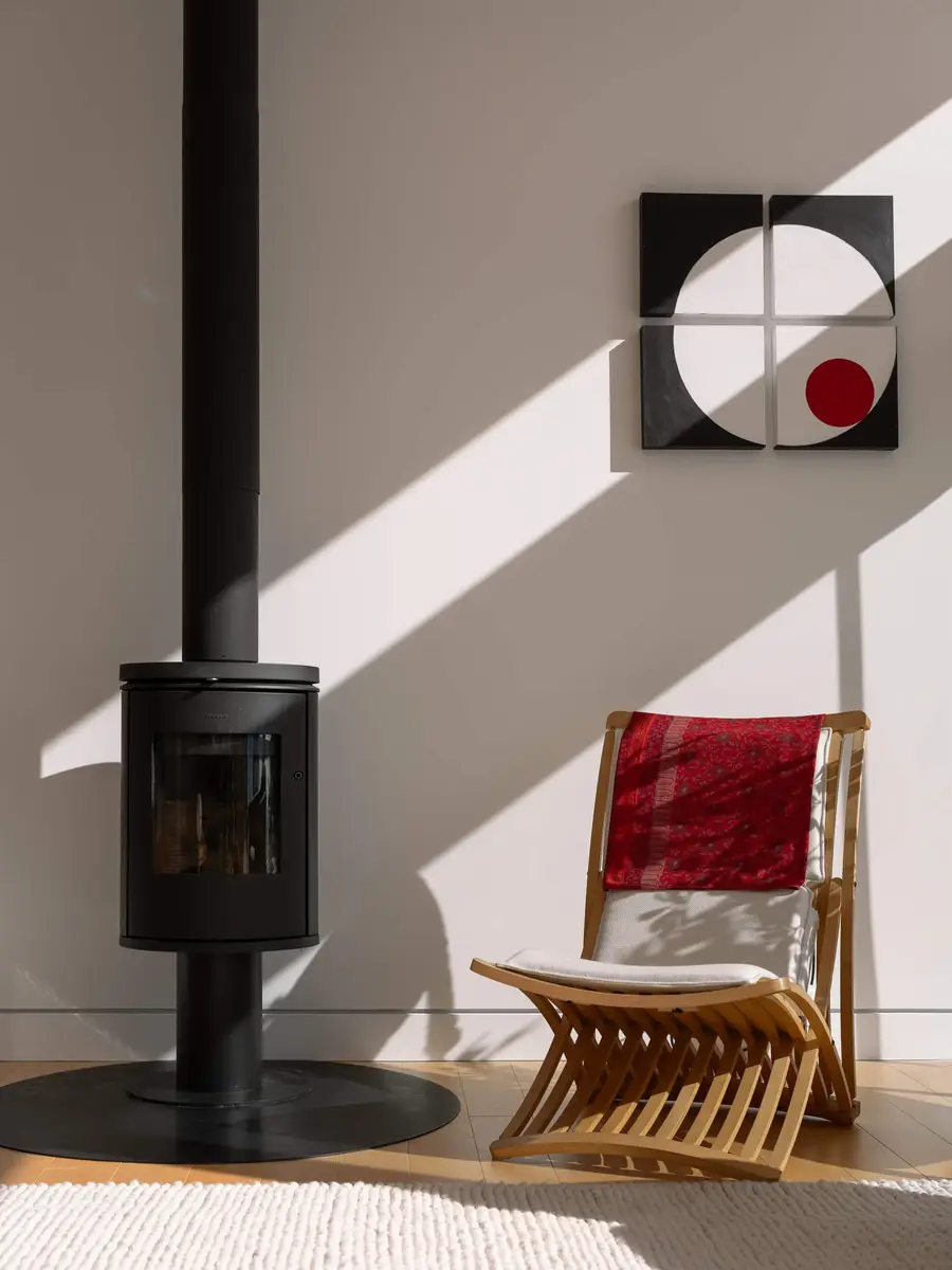 A wood stove below a black and red circle panel, red throw over a slatted chair