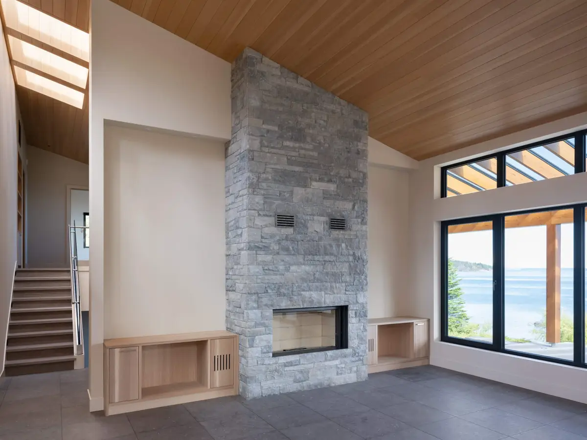 Stone chimney breast under a sloped wood ceiling, the water through the window beside it