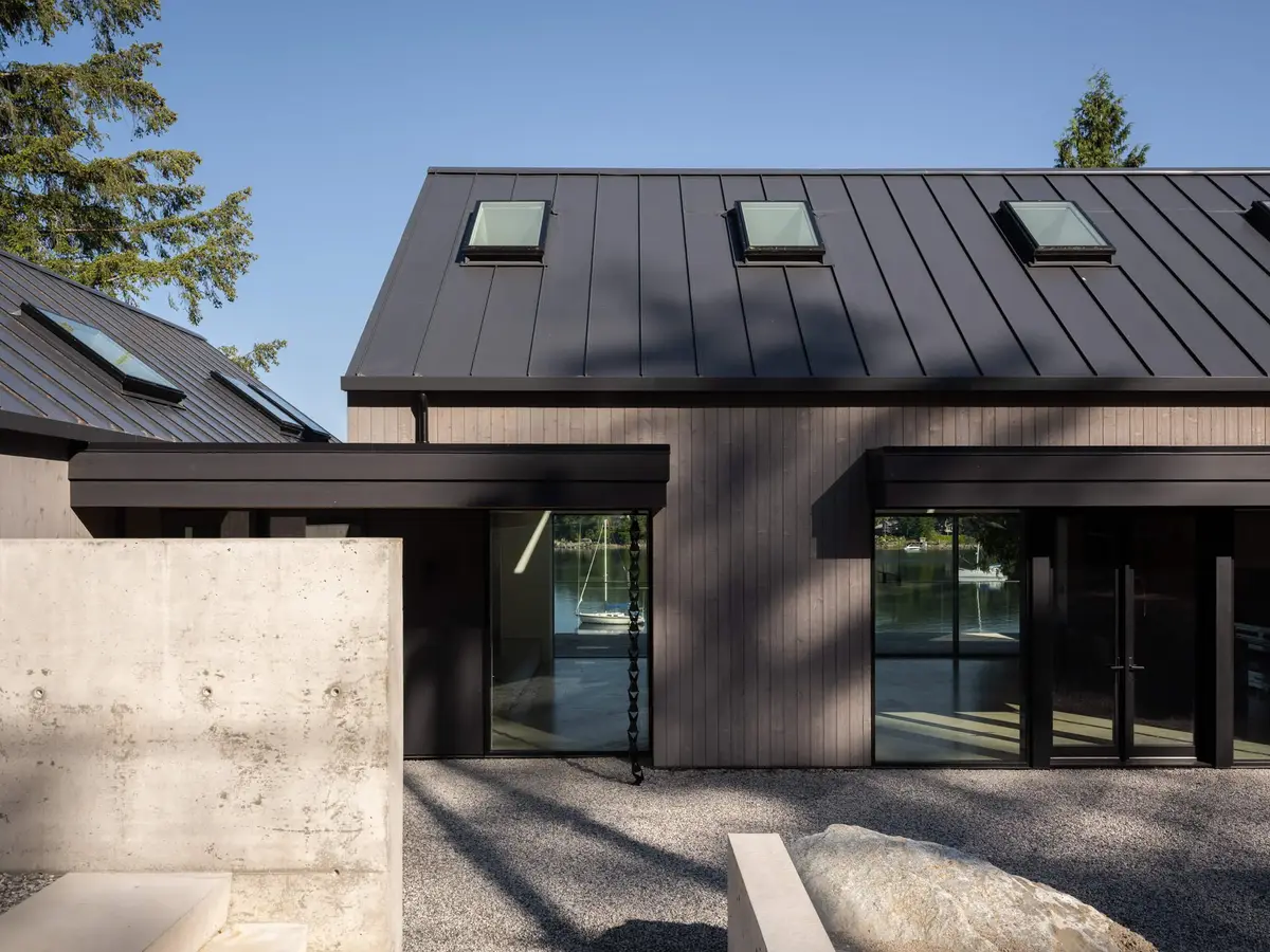 Gravel court behind a concrete wall, glazed doors under a dark ribbed metal roof with skylights