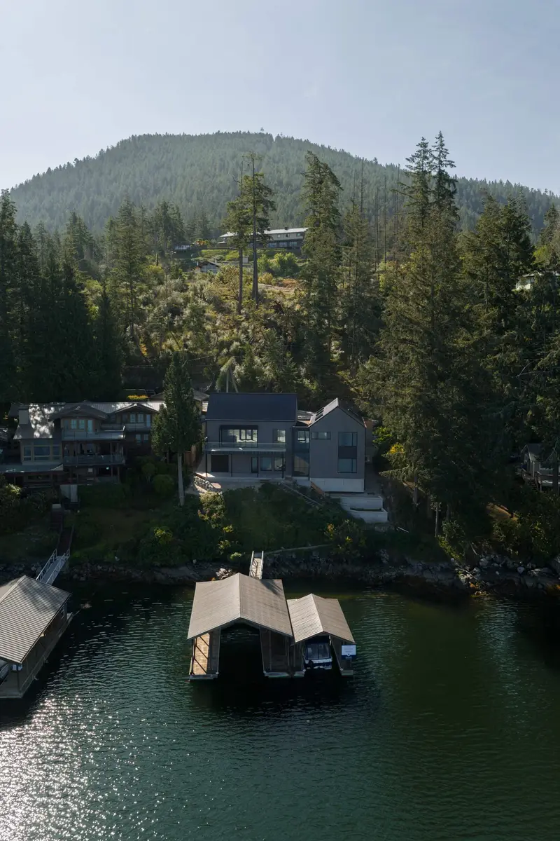 Aerial from the water, a boathouse on the dock below houses set into the trees