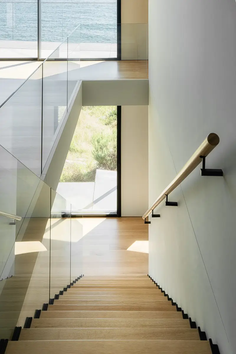 Looking down the steel stair, glass balustrade and a wood handrail against a white wall