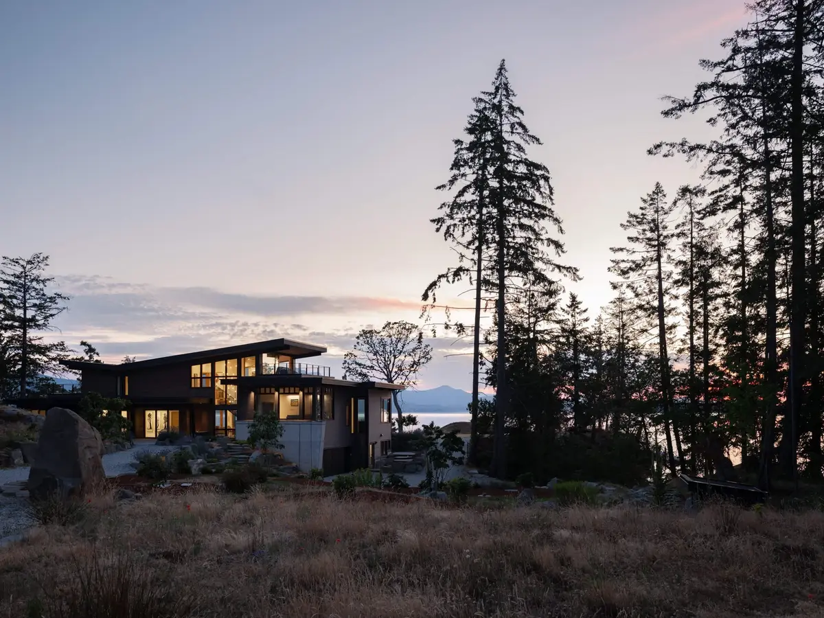 Salt Spring Island residence at dusk among the firs, lit rooms behind the glass