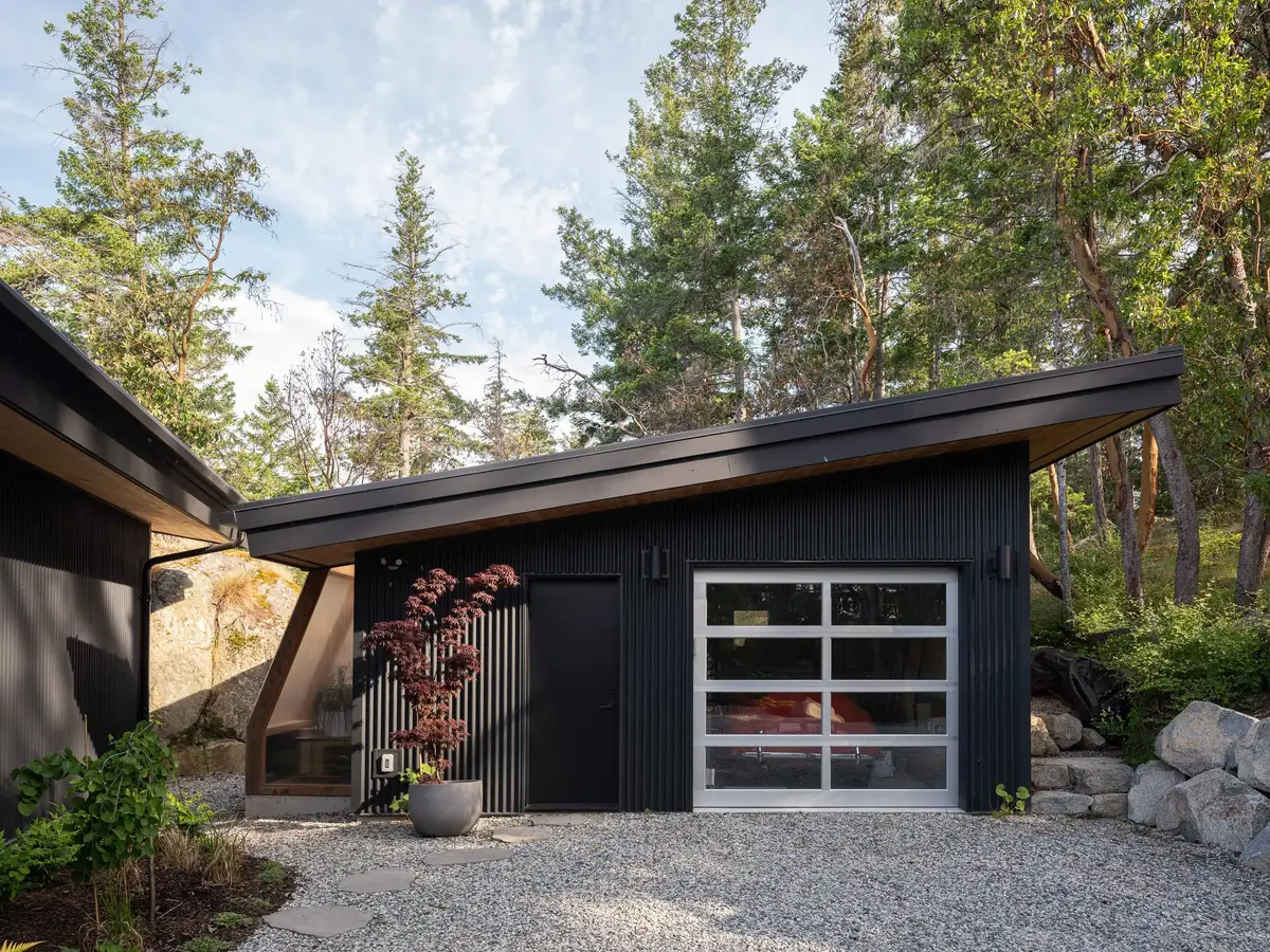 A separate outbuilding in dark cladding with a glazed overhead door onto the gravel
