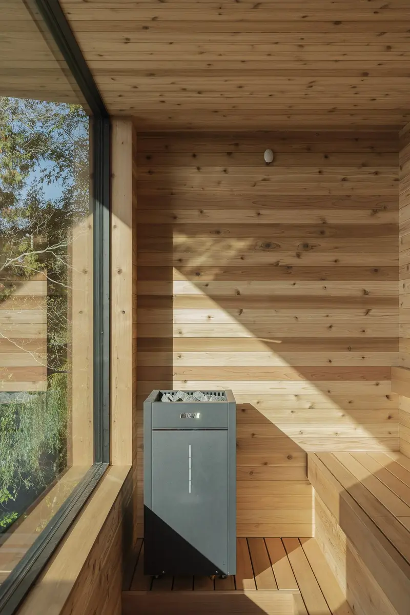 Sauna interior lined in pale wood, heater beside the bench and a window to the trees