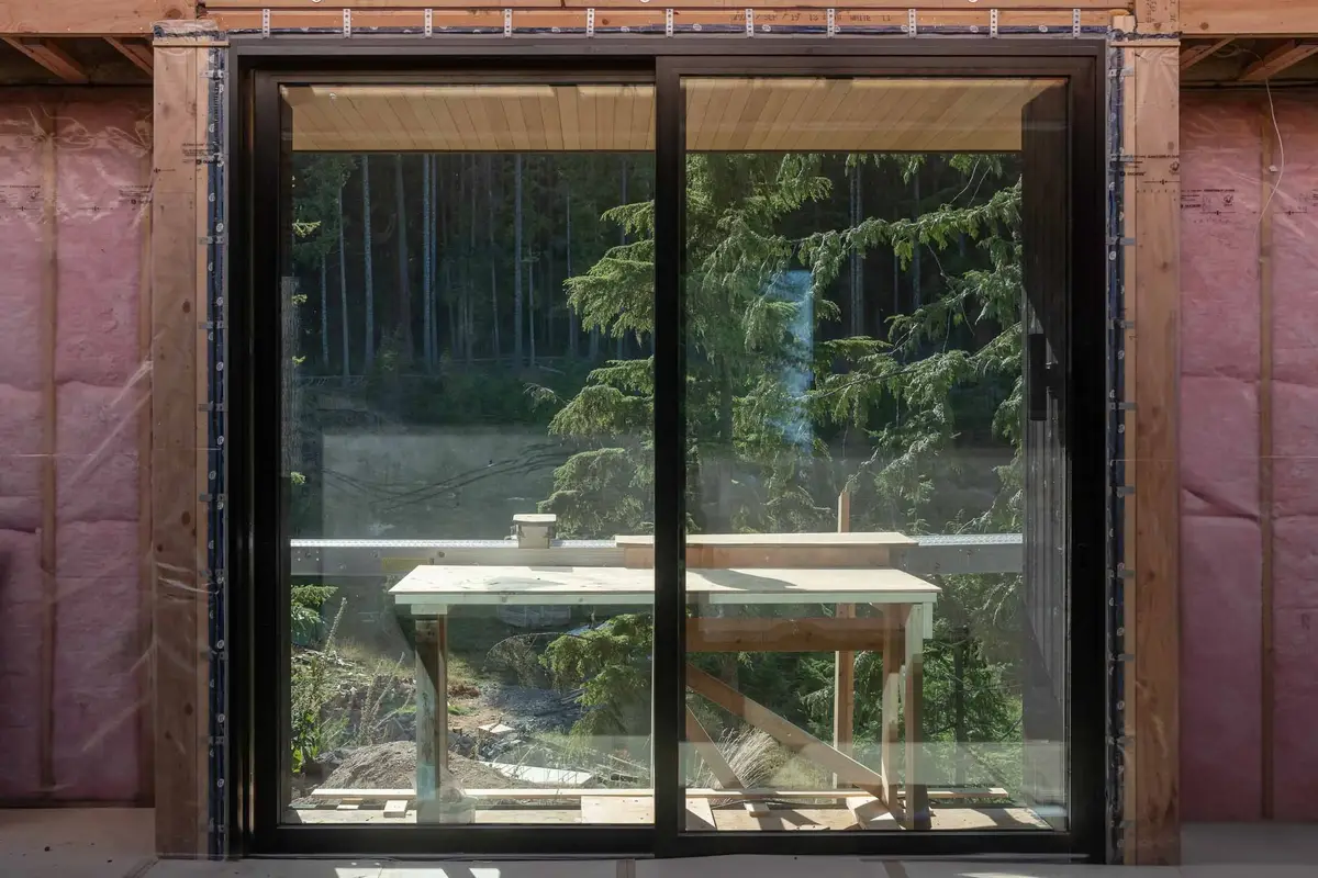 Black sliding door in an unfinished wall with pink insulation, a work table on the deck beyond