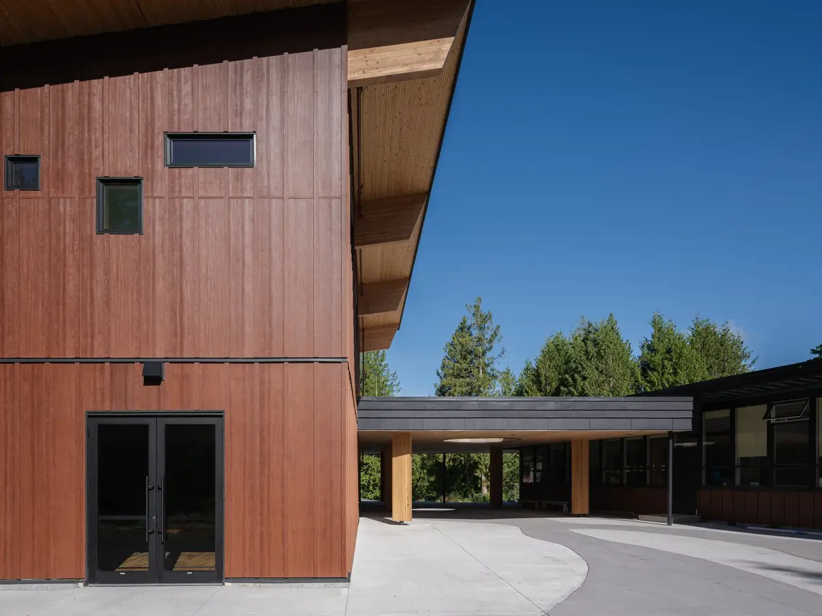 A two storey clad volume meeting the low covered walk under a folded roof