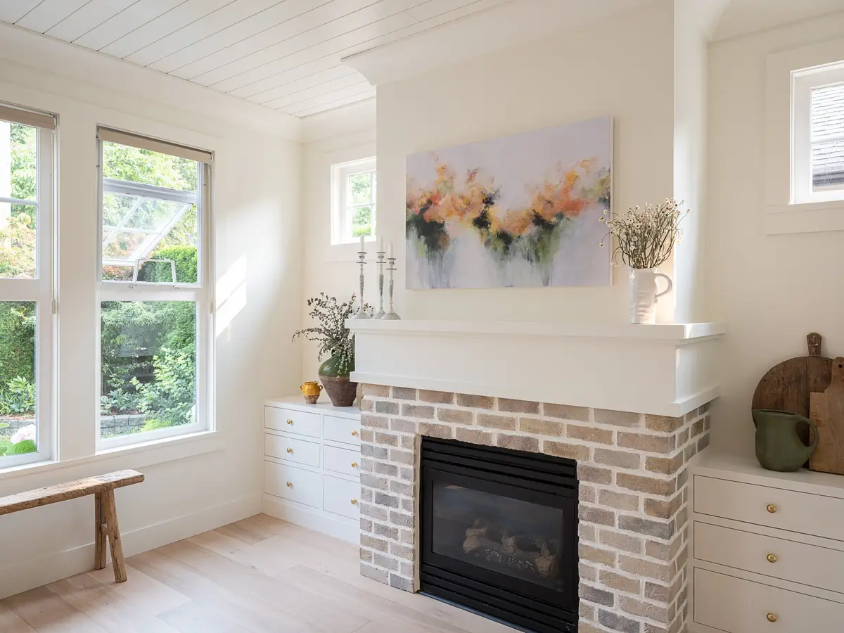 Sitting room with a brick fireplace, a painting above the mantel and windows onto trees