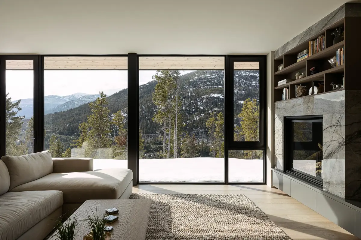 Living room corner, stone fireplace and built in shelving beside full height glazing