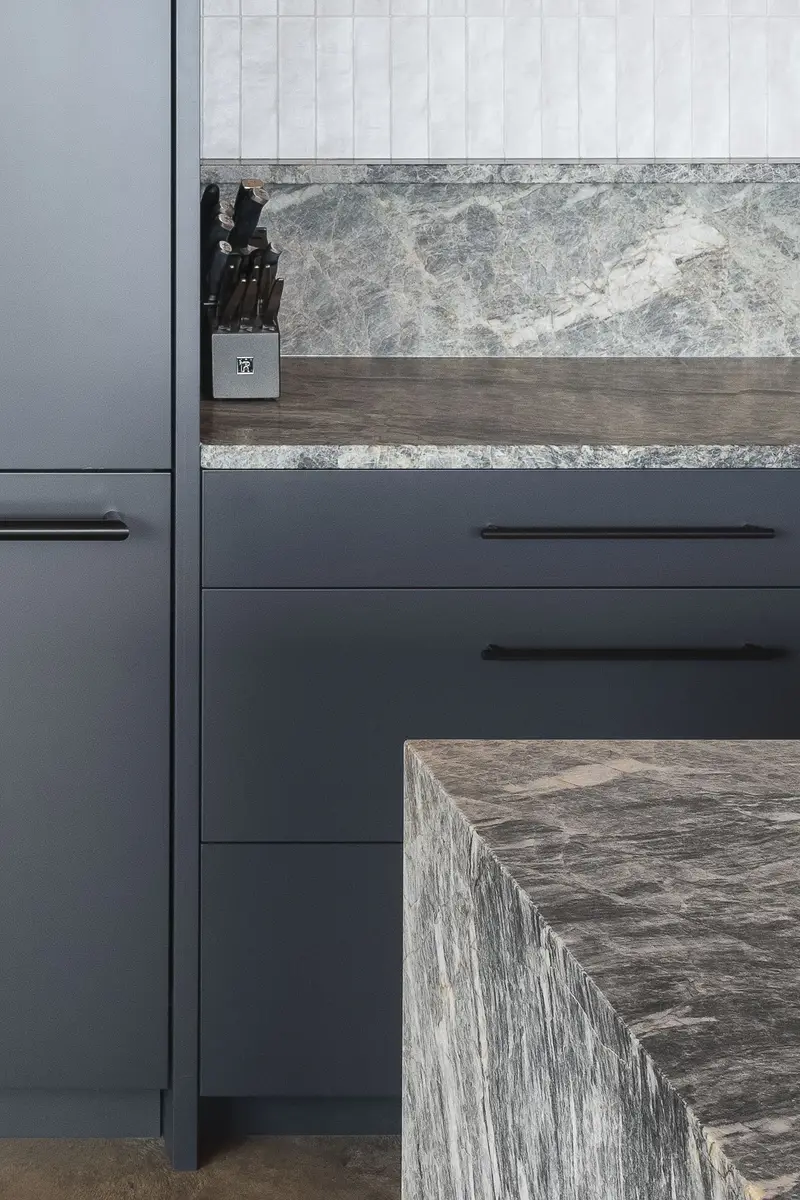 Detail of a knife block on a stone counter beside dark cabinet fronts