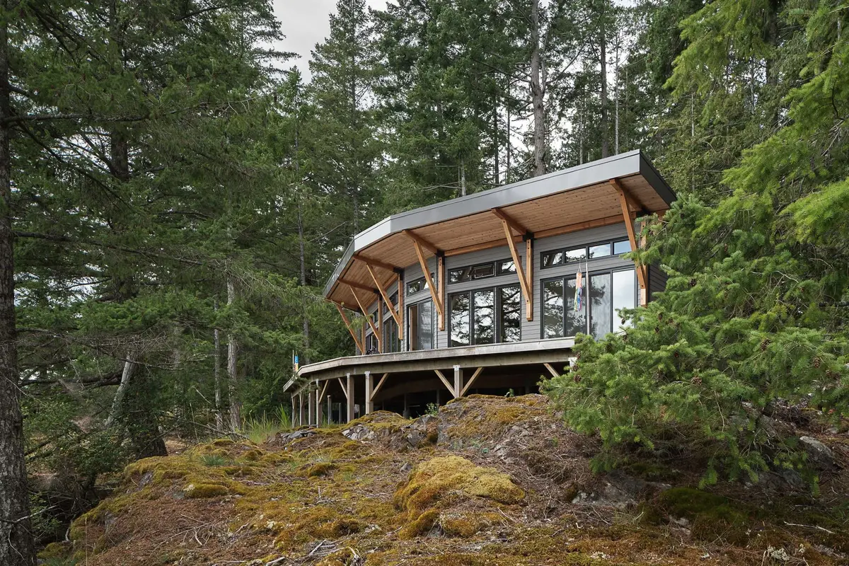 The house on a moss covered rock outcrop, its deck on posts above the drop