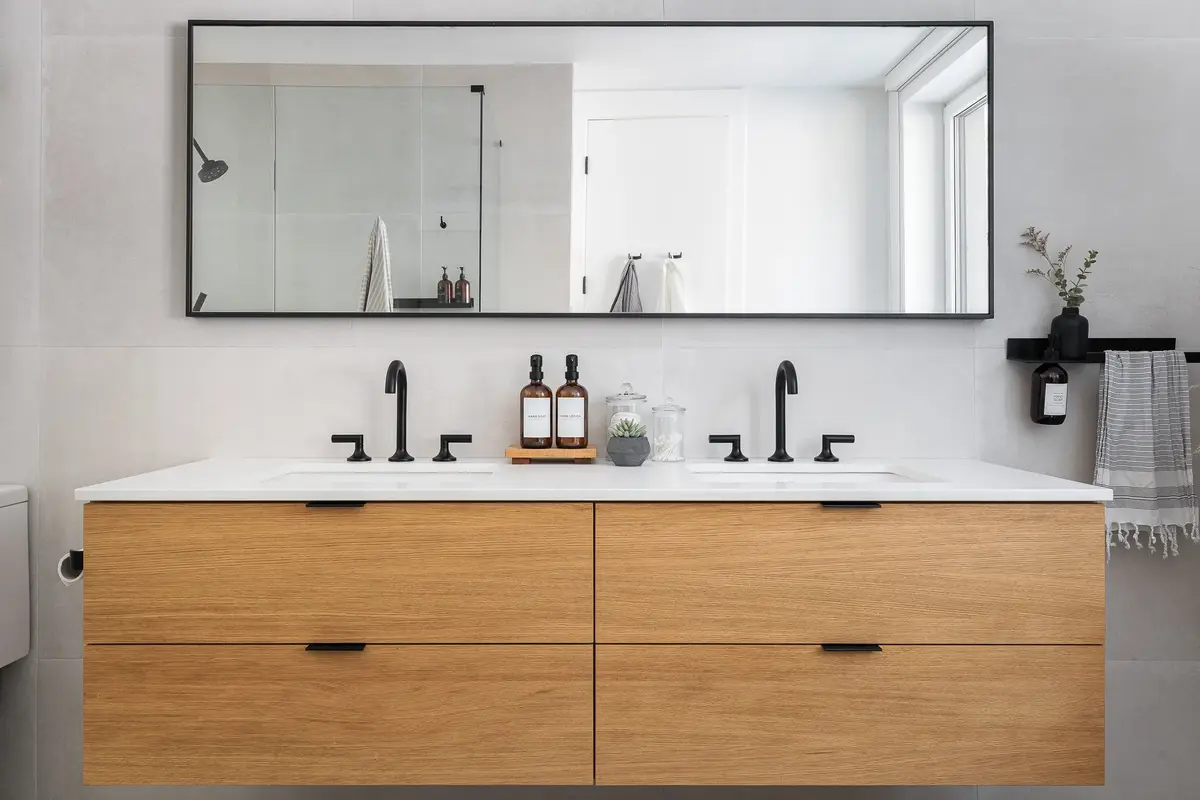 Double vanity in wood below a long black framed mirror, black tapware on a white top