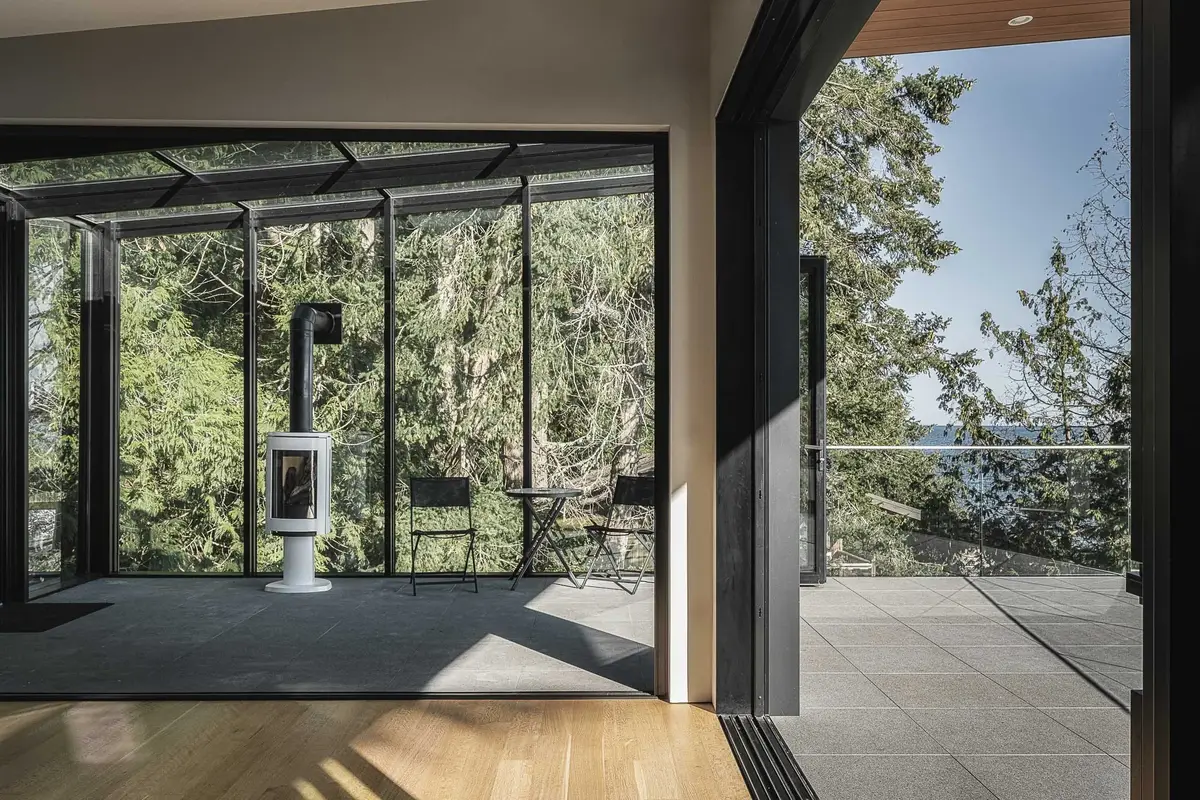 Looking through to a glazed room with a freestanding stove, terrace and water at right