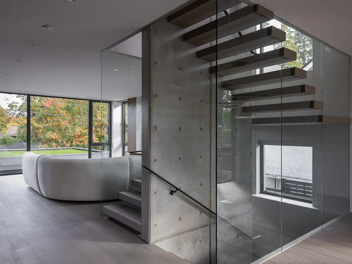 Living room past a concrete wall, floating treads behind glass and a curved sofa