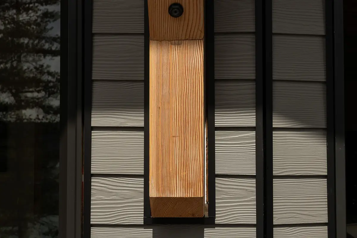 A wide wood post set between dark window frames and textured lap siding
