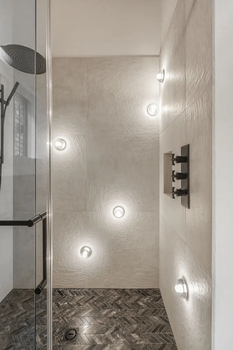 Shower interior in textured tile with a herringbone floor and wall controls