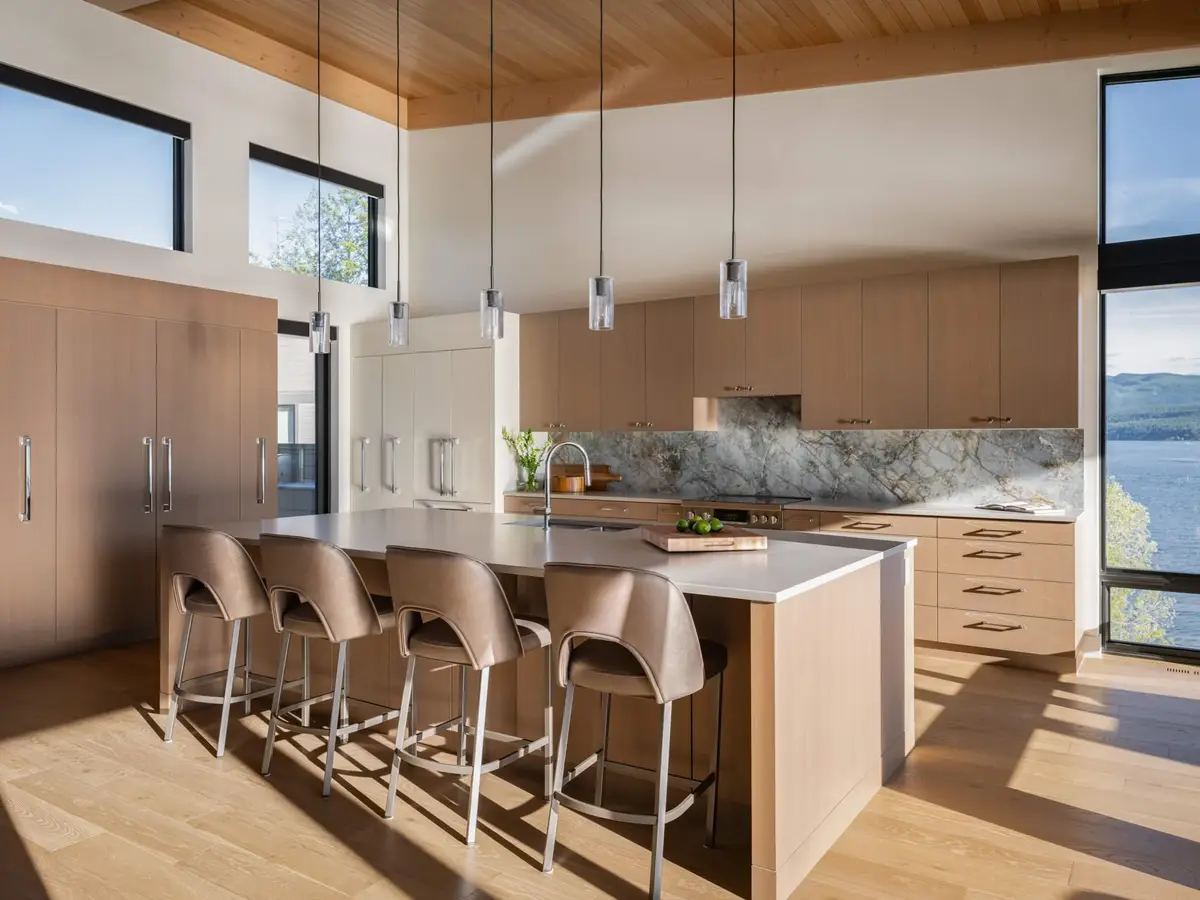Island and stools below a sloped ceiling, clerestory windows above pale wood cabinetry