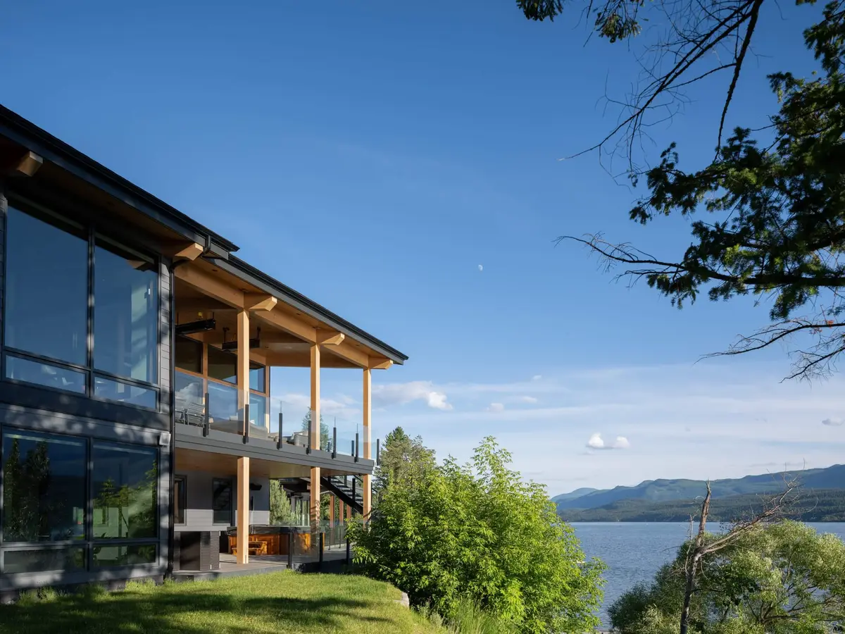 Glazed two storey elevation above a lawn, covered decks on timber posts, lake and mountains beyond