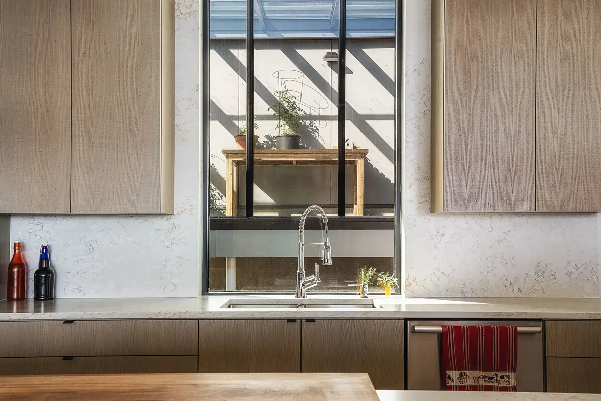 Sink counter under a window, wood cabinets either side and a stone backsplash