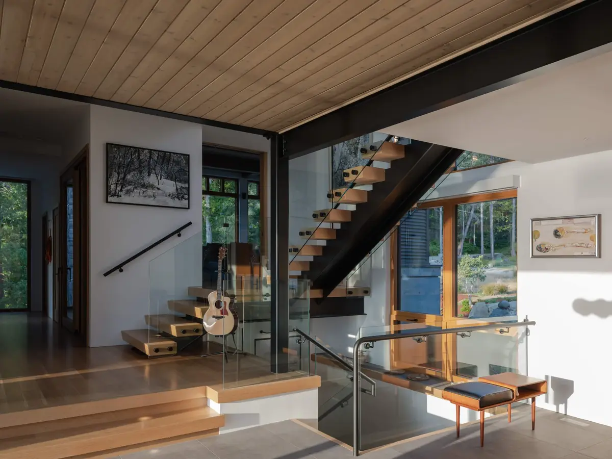 Open stair against a white wall hung with framed works, glazing to the trees