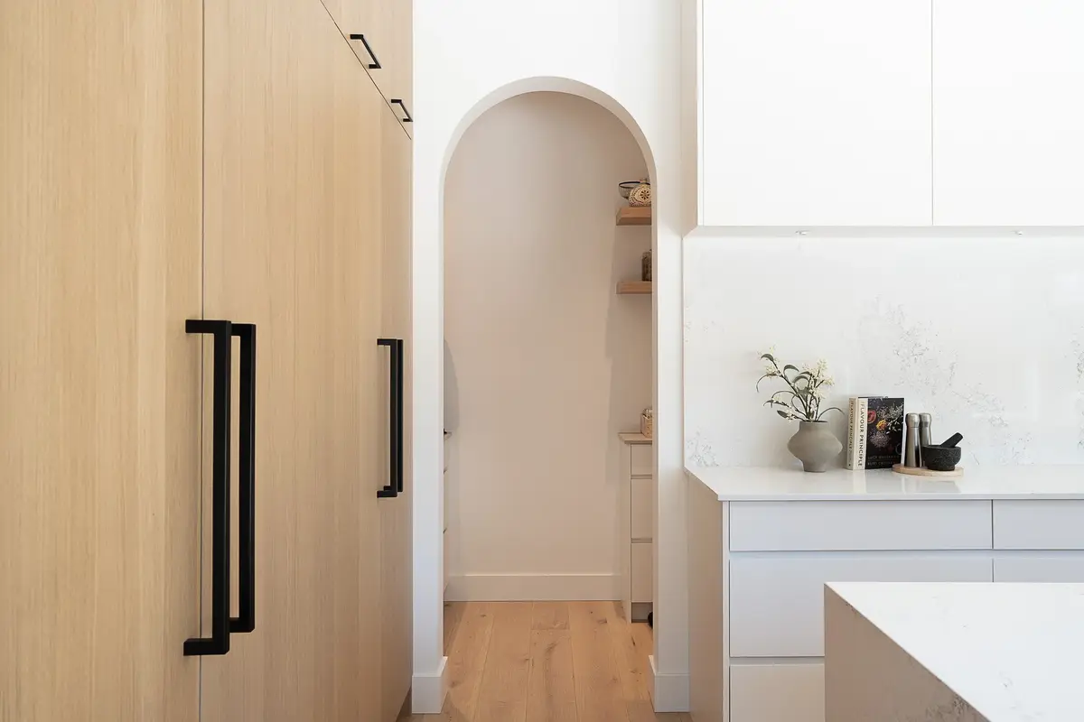 Long black pulls on tall wood doors beside an arched opening into the pantry
