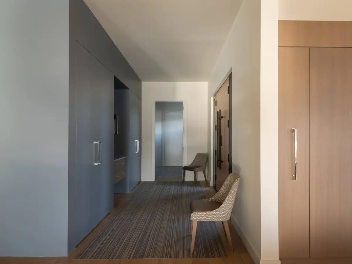 Corridor with a dark blue wall of millwork opposite tall wood cabinetry, striped runner underfoot