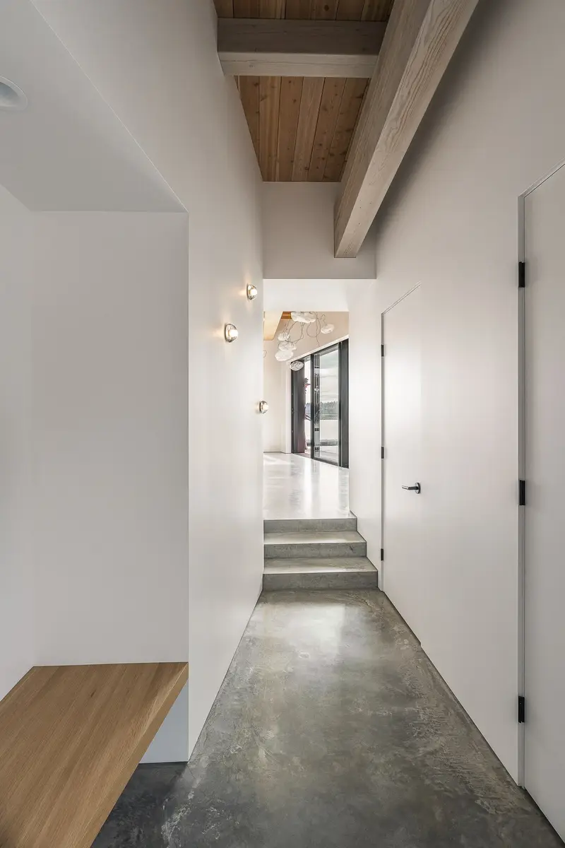 A hall with a floating wood bench, concrete floor and steps at the far end