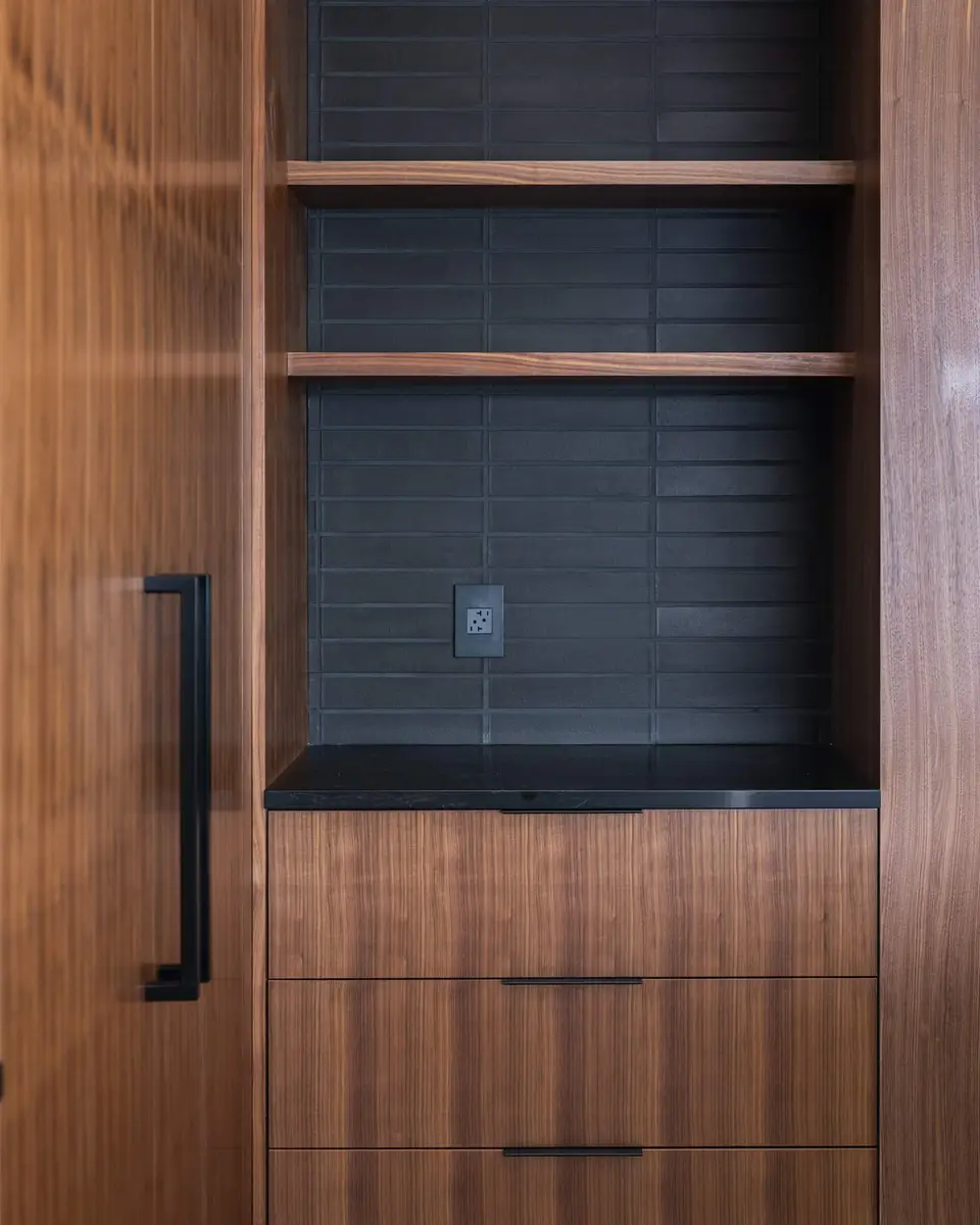 Pantry shelves in wood against dark tile, drawers below and a tall door at left