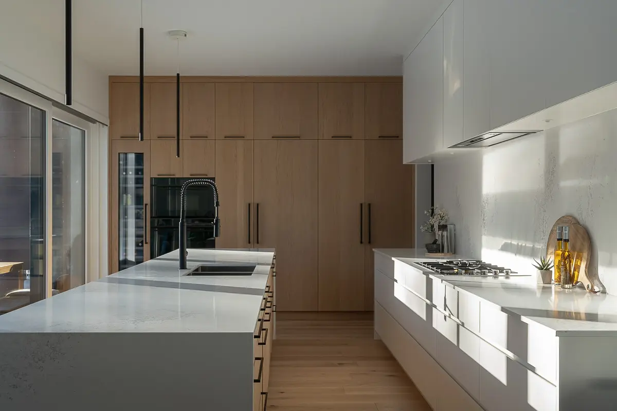 Looking down the kitchen past a pale stone island to full height wood cabinetry